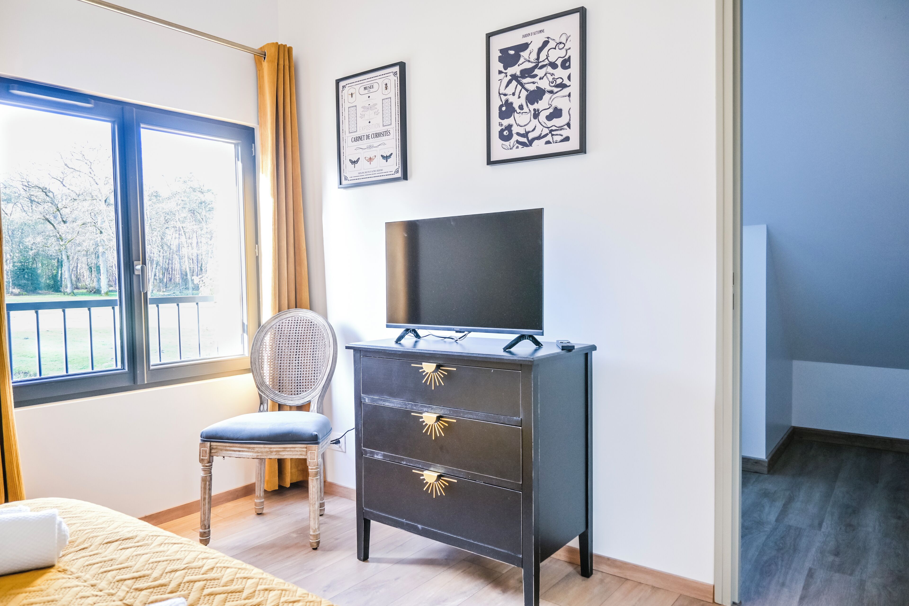 Un dormitorio con una cama, un aparador, una silla, un televisor y dos cuadros en la pared.