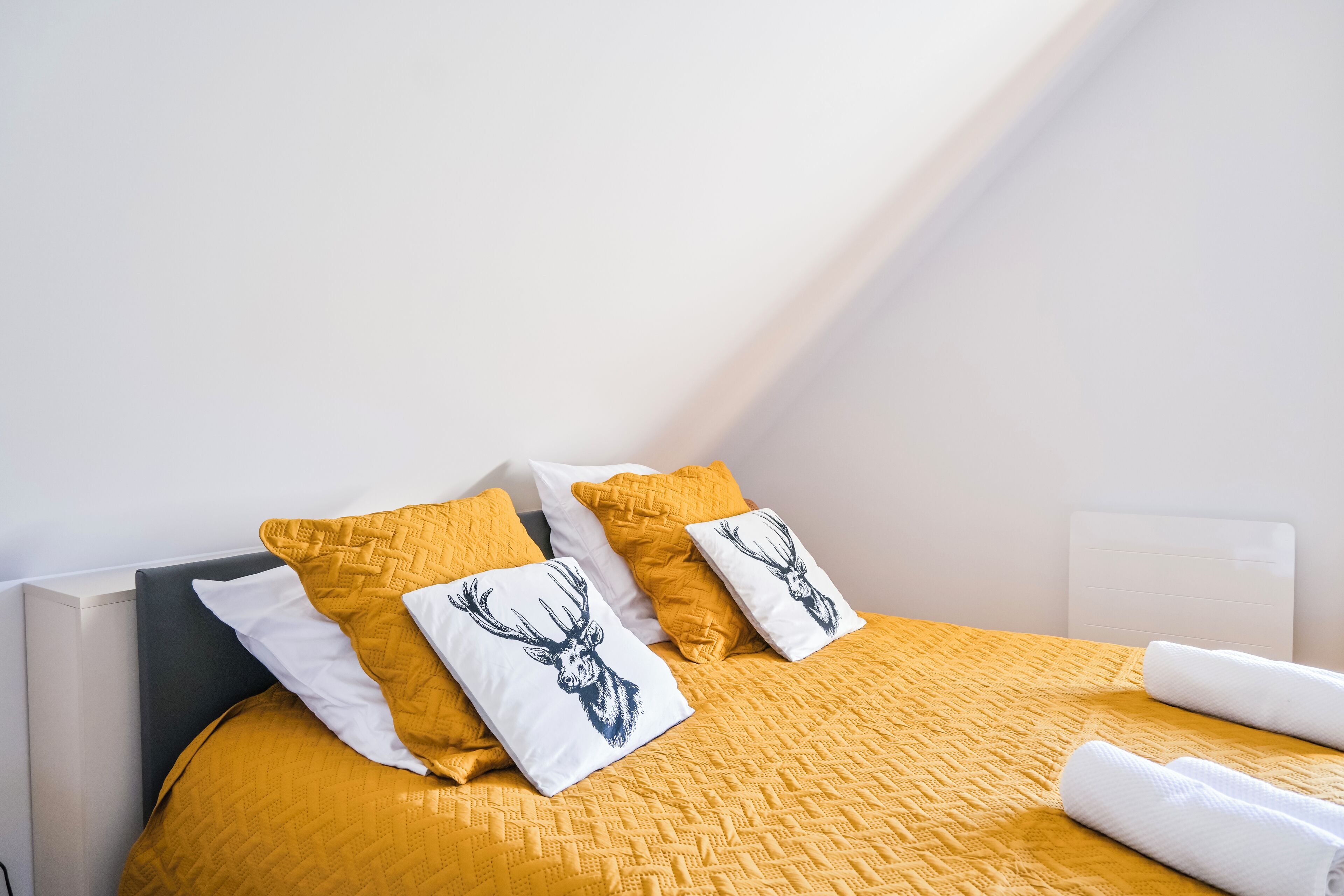 A bed with a yellow quilt, white pillows with deer prints, and a white headboard.