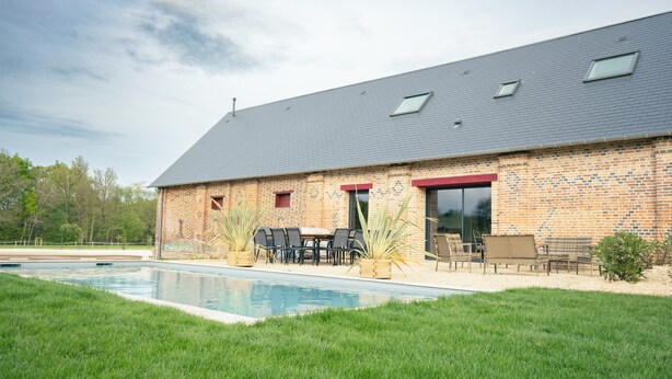 A brick building with a swimming pool, outdoor seating, and a red door. - Les Longères de Montfranc (Pierrefitte-sur-Sauldre)