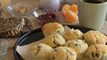 Una bandeja con muffins y galletas sobre una mesa, junto a una taza de café y un bol de fruta.