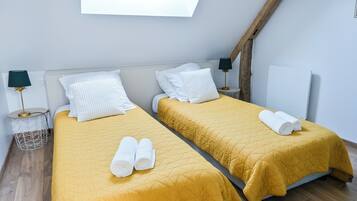 Habitación con dos camas, cada una con colcha amarilla acolchada y almohadas blancas. Hay toallas enrolladas sobre las camas y un tragaluz arriba.
