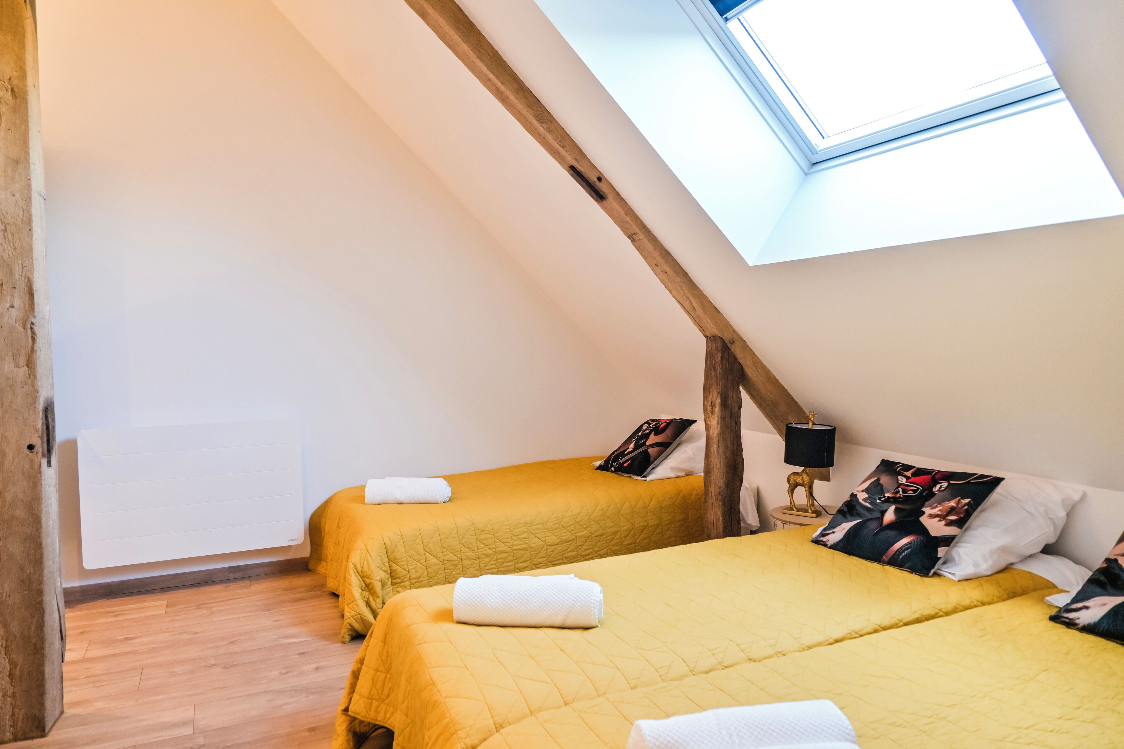 Una habitación con dos camas, un tragaluz, vigas de madera y un radiador.