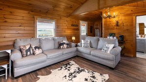 A cozy log cabin interior with a sectional sofa, a chandelier, and a view of the outdoors. - The Ridge Cabin! 15-minutes from the ARK (Williamstown)