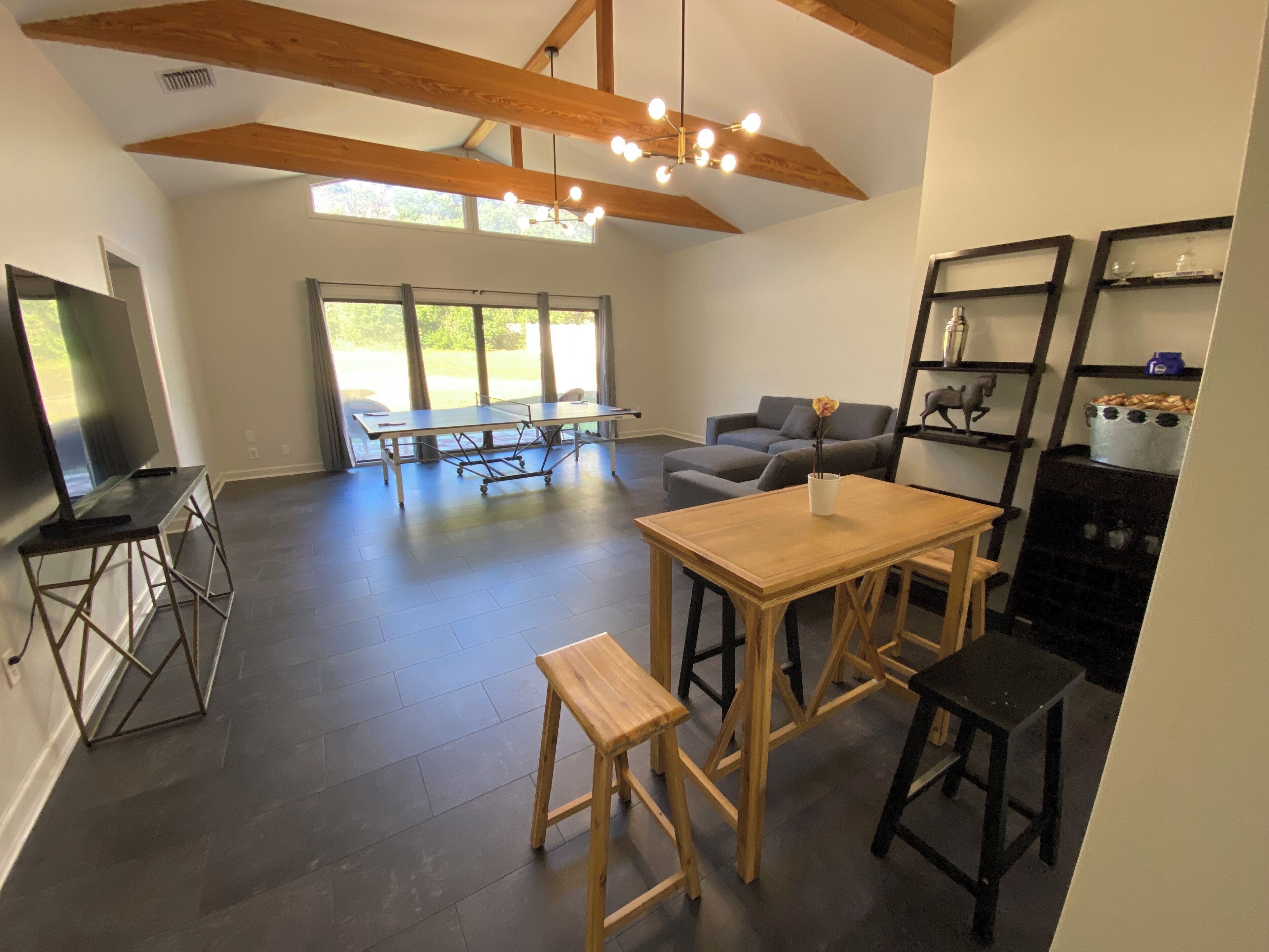 A spacious living area with a wooden table, a sofa, a TV, and a large window.