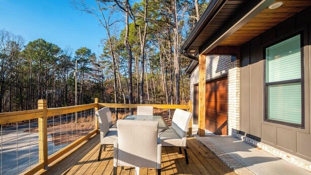 Um deck de madeira com mobiliário externo, com vista para uma área arborizada.