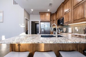 A modern kitchen with wooden cabinets, a stainless steel refrigerator, and a granite countertop.