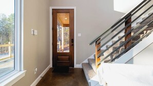 Um corredor com porta de madeira que dá para um deck, escada com corrimão de metal e piso coberto de carpete.
