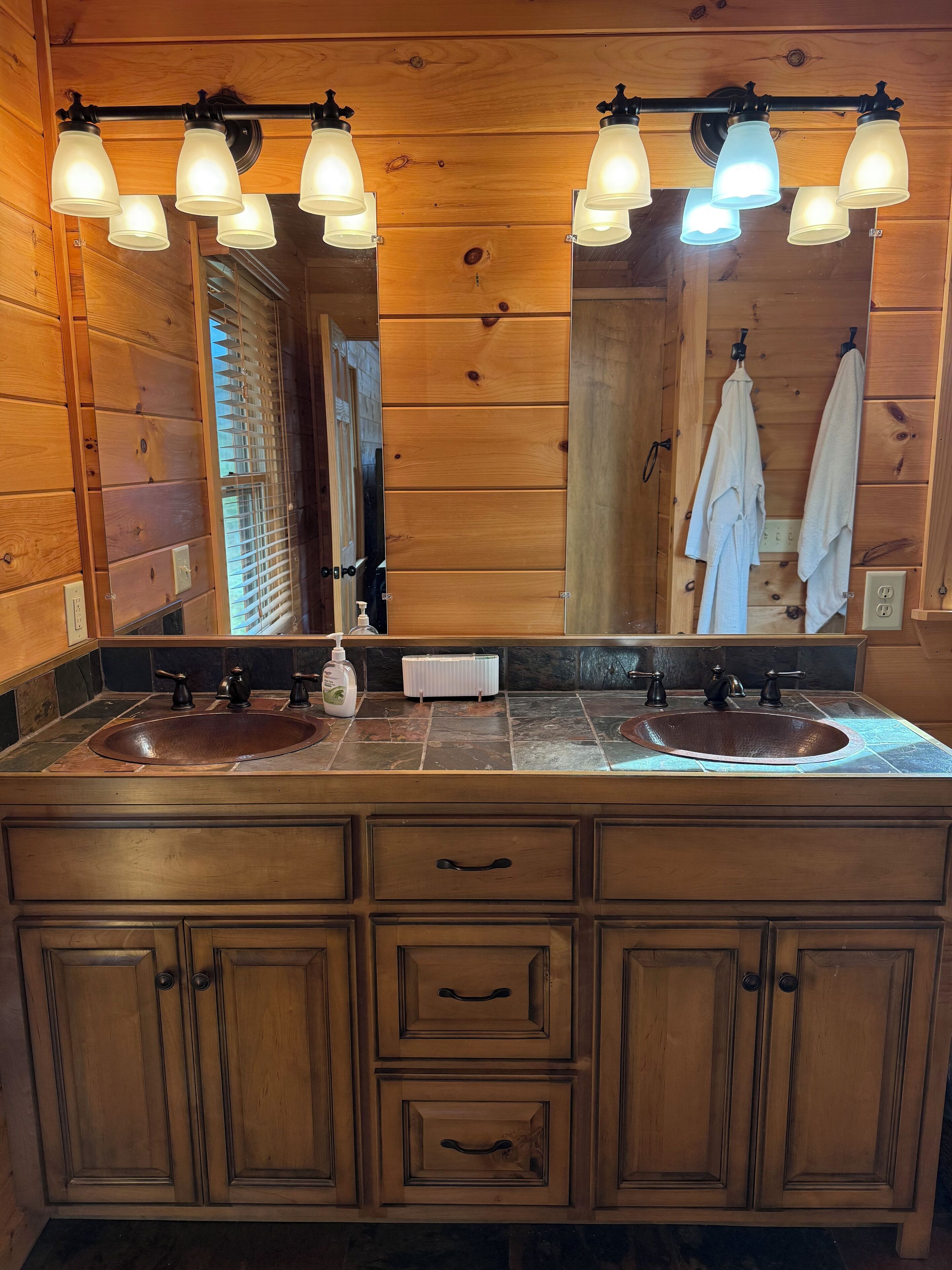 A wooden bathroom with a large mirror, two sinks, and a towel rack.