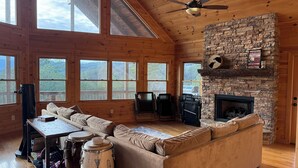 A spacious living room with a stone fireplace, large windows, and a high ceiling fan. - Gorgeous Cabin Private Retreat on 15 acres (Copperhill)