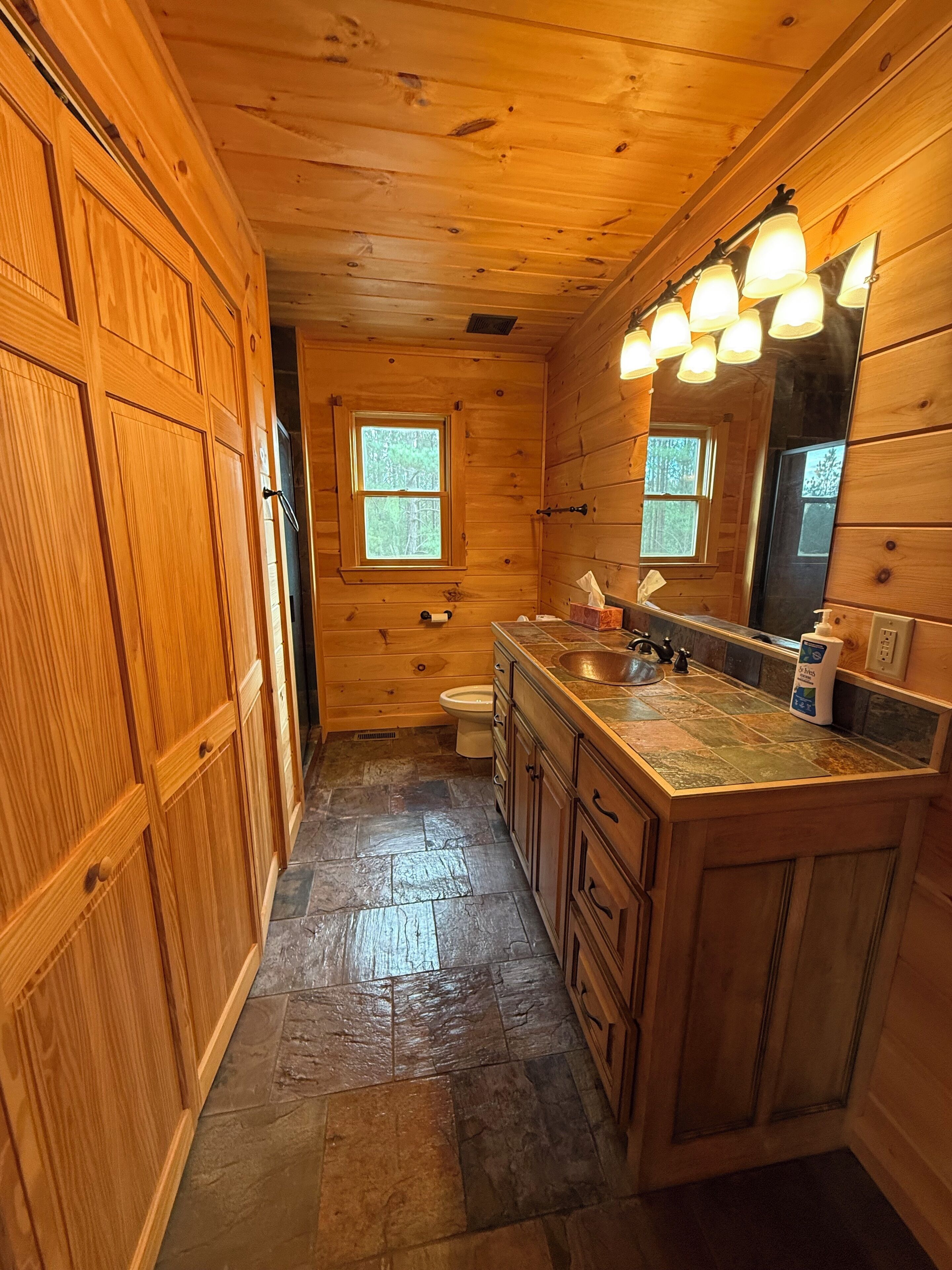 A wooden cabin bathroom with a stone-tiled floor, a sink with a mirror, and a toilet.