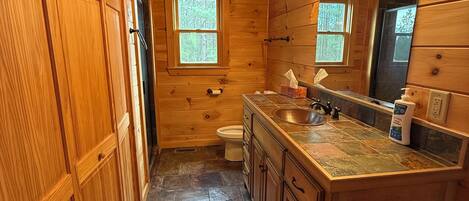 A wooden cabin bathroom with a stone-tiled floor, a sink with a mirror, and a toilet.