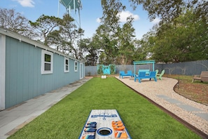 Un giardino con tavolo da shuffleboard, un capanno blu e un patio in legno.