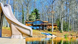 A cabin with a wooden deck, a slide, and a lake. - Lakefront Lake Anna Views, Dock, Hot Tub, Firepit (Bumpass)