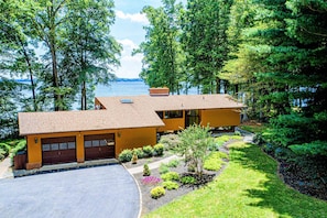 A two-story house with a garage, surrounded by lush greenery and a view of a lake. - Lakefront Lake Anna Views, Dock, Hot Tub, Firepit (Bumpass)
