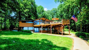 A modern two-story house with a deck, surrounded by lush greenery. - Lakefront Lake Anna Views, Dock, Hot Tub, Firepit (Bumpass)