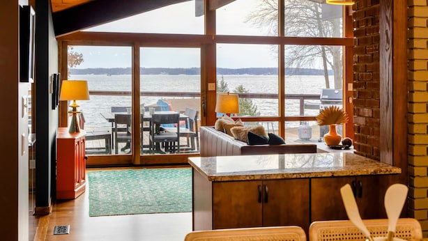 A room with a large window overlooking a body of water, a wooden ceiling, and a seating area with a table and chairs. - Lakefront Lake Anna Views, Dock, Hot Tub, Firepit (Bumpass)