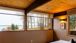 A bedroom with a large window, a bed, and a wall-mounted light fixture. - Lakefront Lake Anna Views, Dock, Hot Tub, Firepit (Bumpass)