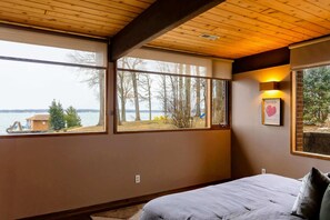 A bedroom with a large window, wooden ceiling, and a bed with pillows.