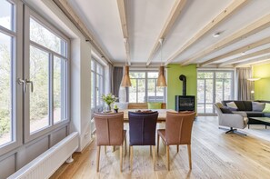 A modern dining area with a wooden table, four chairs, and a bench. There are large windows on one side and a fireplace on the opposite wall. - Barrier-free 5* apartment Bergmannstrost 120 sqm with high-quality natural materials (Sankt Andreasberg)
