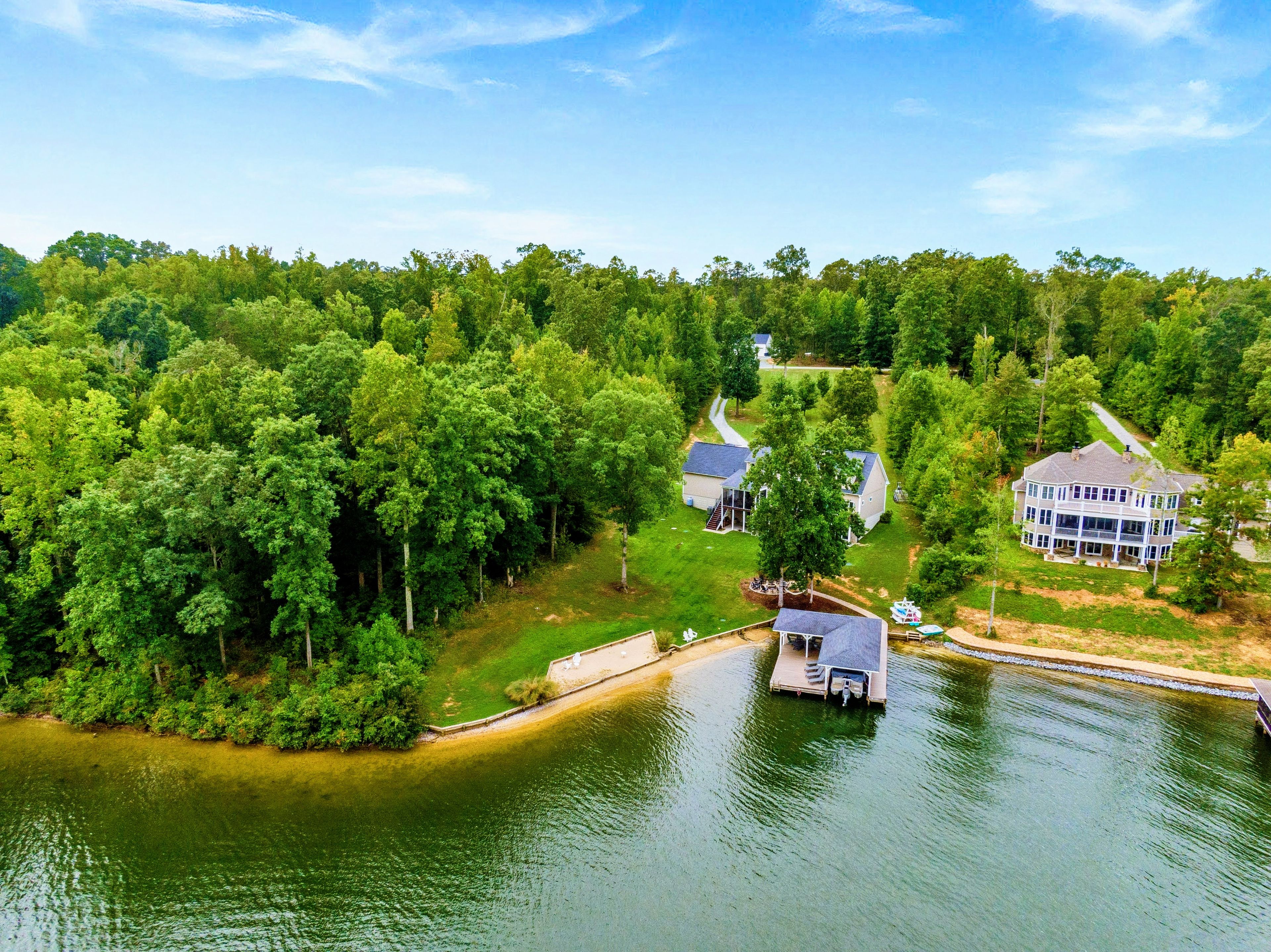 A lakeside property with a dock, a large house, and a smaller building, surrounded by dense greenery.