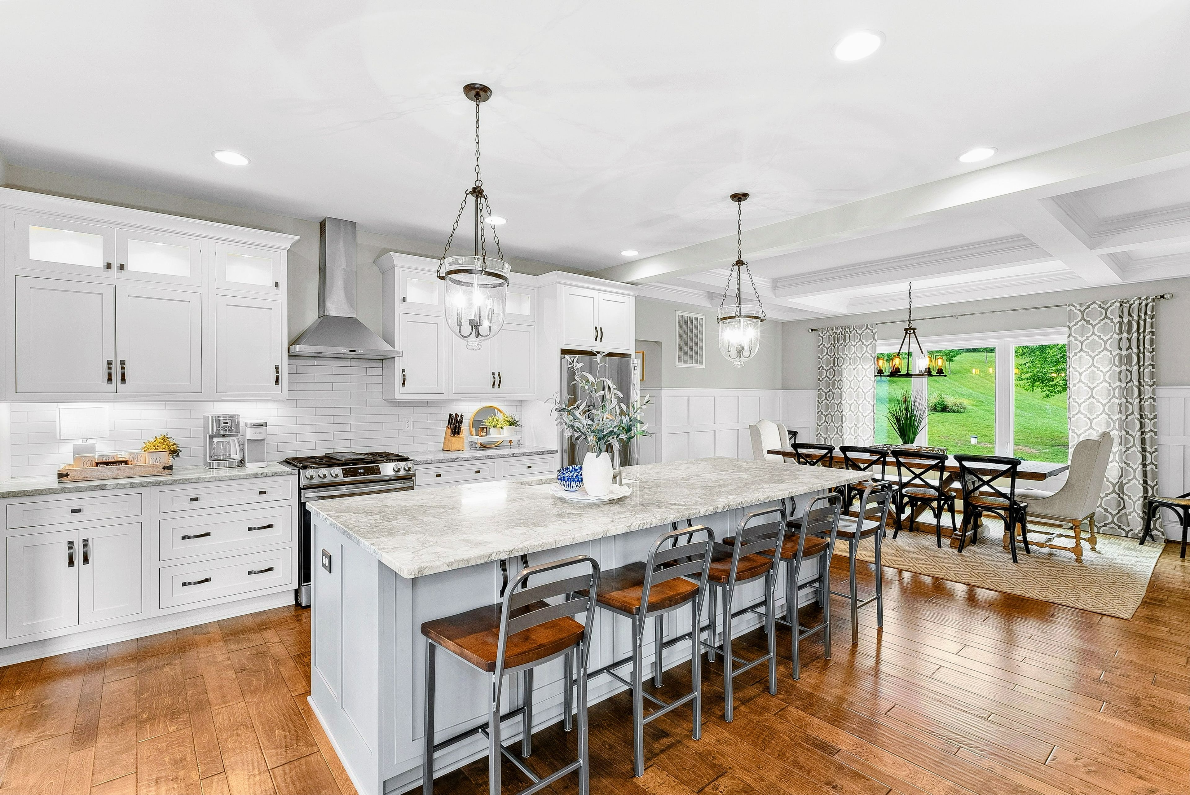A modern kitchen with white cabinetry, a large island with bar stools, and pendant lighting.