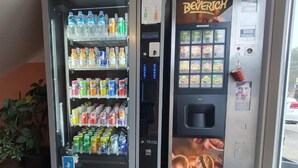 Two beverage vending machines with a variety of drinks and a coffee-themed advertisement. - Akdeniz Pension (Ludwigsfelde)