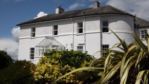 A two-story white building with a conservatory, surrounded by greenery. - Hill House – Luxury Group Getaway with Stunning Views, Sleeps 17 (Cashel)