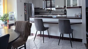 A modern kitchen with white cabinets, a built-in oven, and a dining area with two chairs and a table. - Large private bungalow in Lévis (Saint-Nicolas)