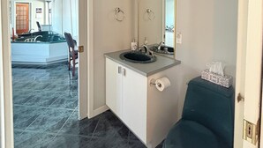 A bathroom with a sink, mirror, and toilet. There is a chair and a towel dispenser. The floor is tiled. - Large private bungalow in Lévis (Saint-Nicolas)