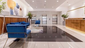 A modern lobby with a blue sofa, a reception desk, and a marble floor. - Designer One Bed Apt | No Loadshedding (Cape Town)