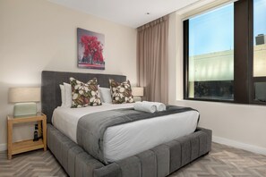 Relax in a spacious room with a large bed, wooden nightstand, and city view.
