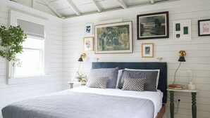 A bedroom with a bed, a nightstand, a lamp, a window with blinds, and wall art. - New listing! Cozy, fresh and clean 1-bedroom cottage with Pond access in Chatham (Chatham)