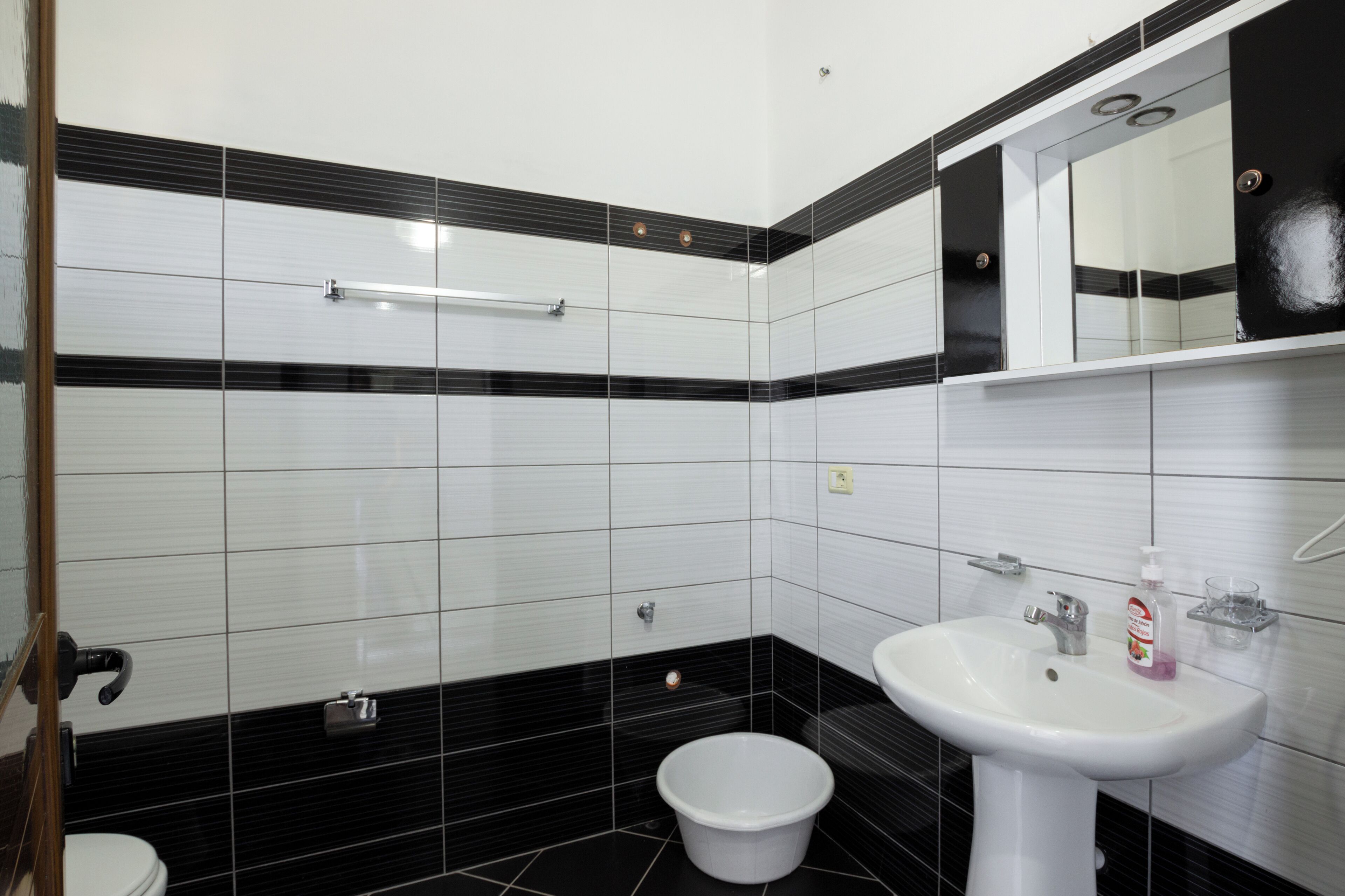 A bathroom with white and black tiles, a white sink, a mirror, and a toilet.