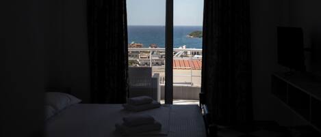 Une chambre d’hôtel avec un lit, une télévision et une vue sur la mer et une île lointaine.