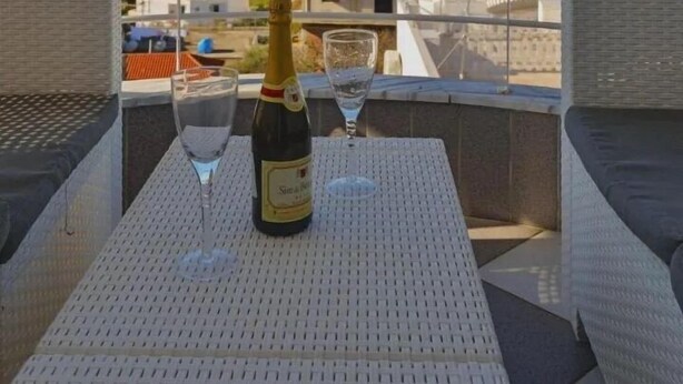 Ein Balkon mit Tisch für zwei Personen, einer Champagnerflasche und einem Glas. Der Balkon bietet Blick auf eine Stadtlandschaft mit Gebäuden und blauem Himmel.