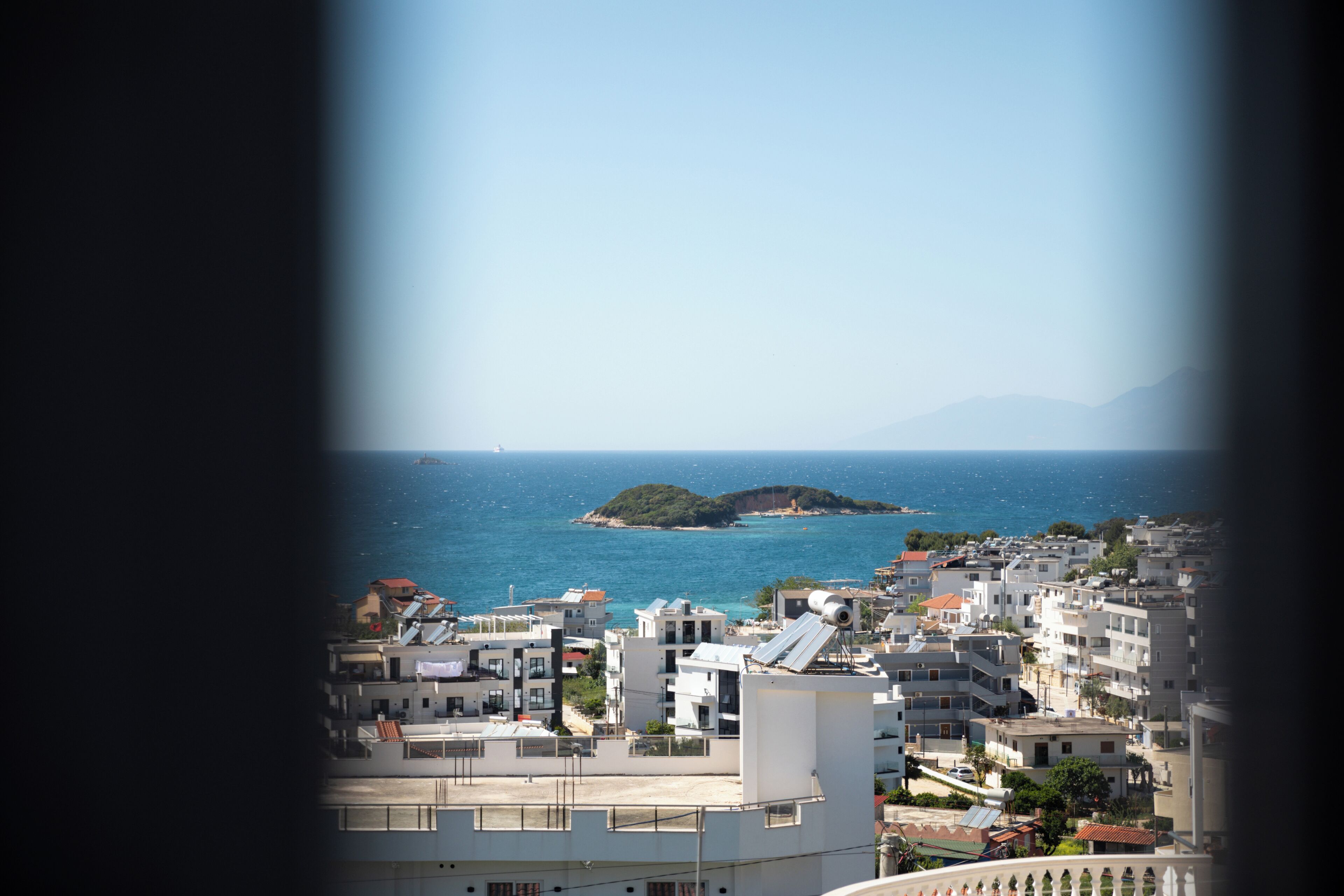 Un paisaje urbano costero con edificios modernos, una vista despejada del mar y una isla distante.