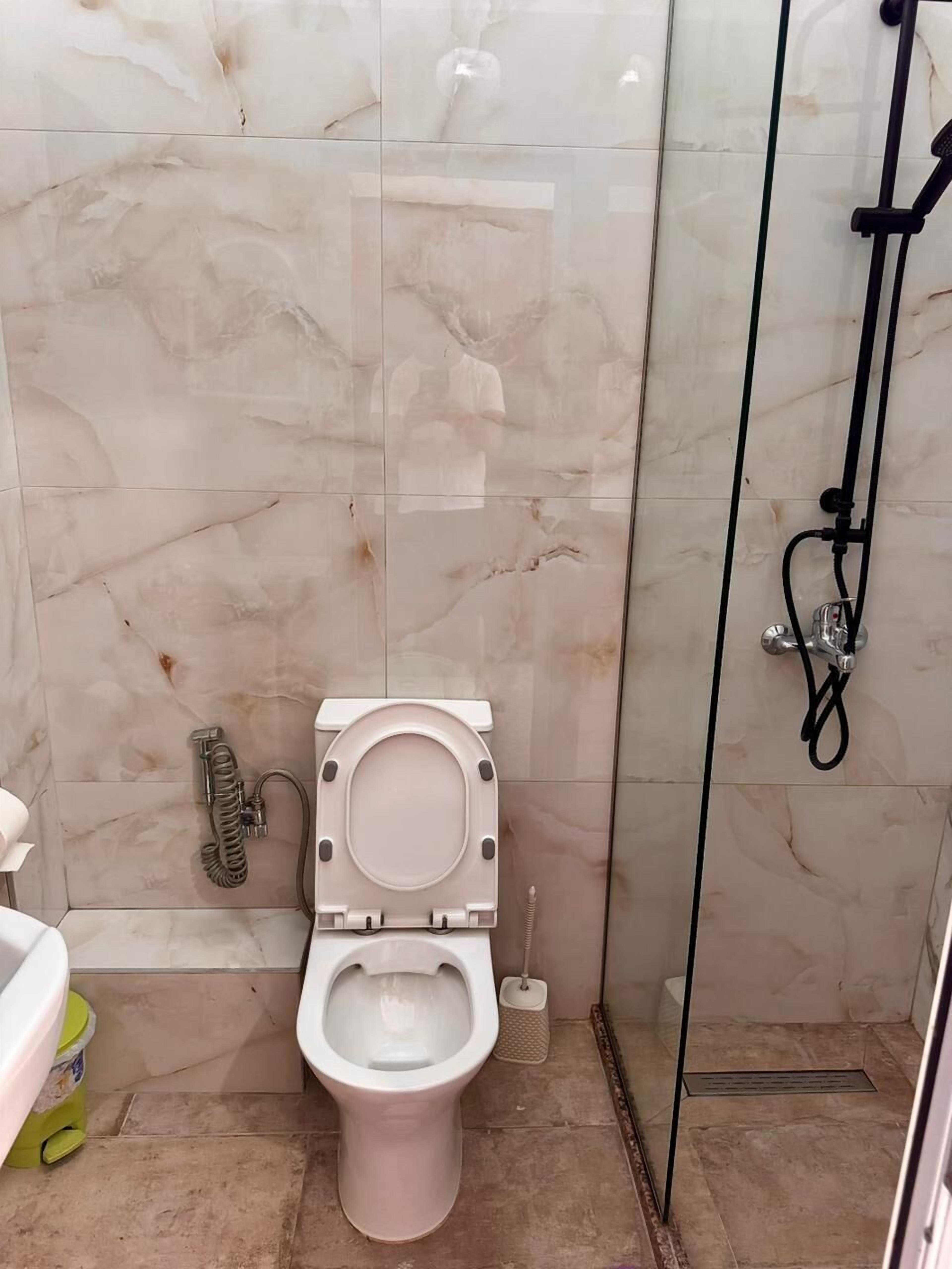 Een badkamer met een toilet, een douche en een douchecabine met glazen wanden.