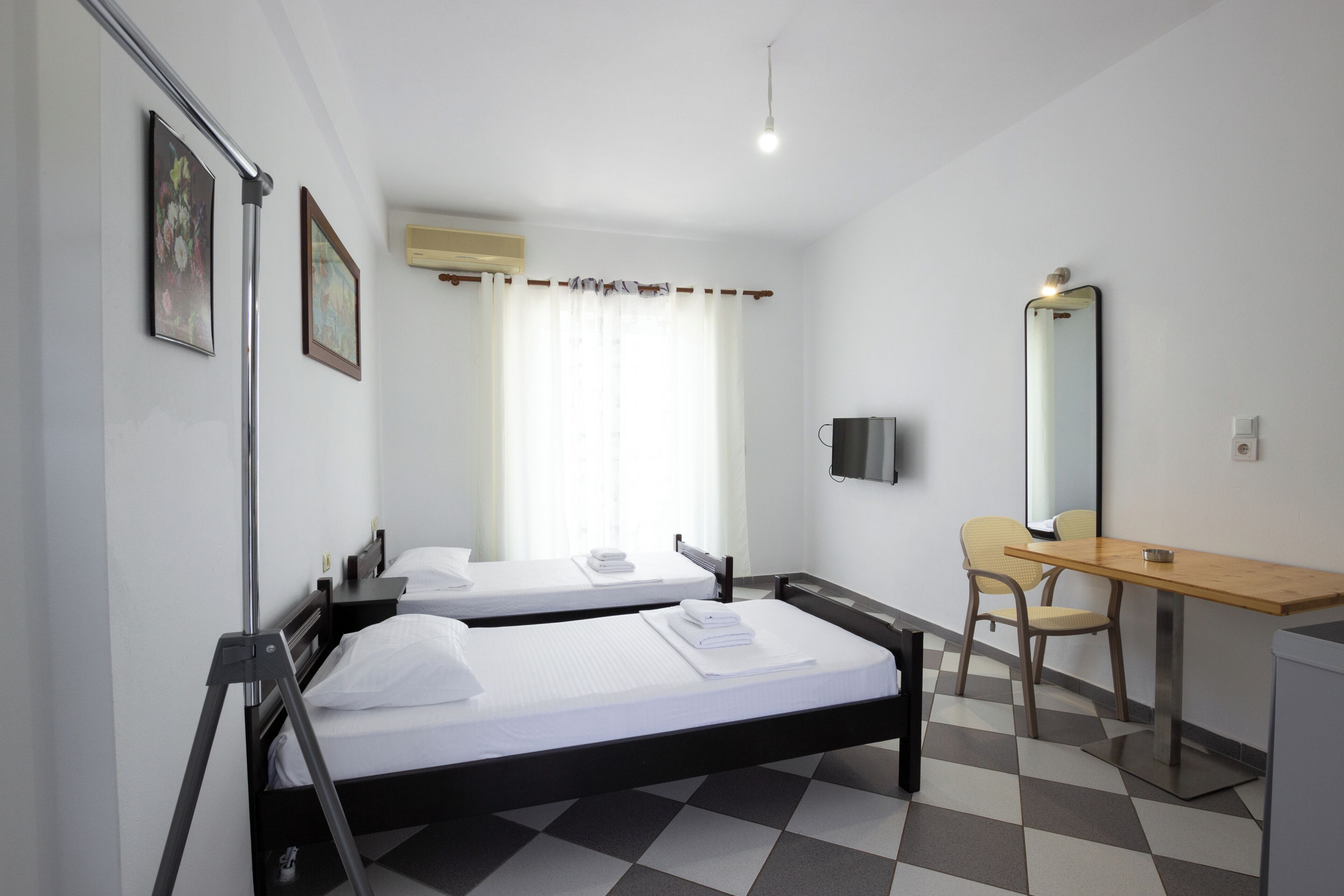 A hotel room with two beds, a desk, a chair, a television, and a mirror.
