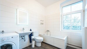 Moderni kylpyhuone, jossa on pesukone, wc, pesuallas ja kylpyamme.