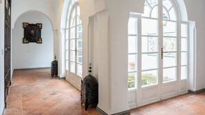 Um corredor com janelas em arco, piso ladrilhado e luminárias decorativas.