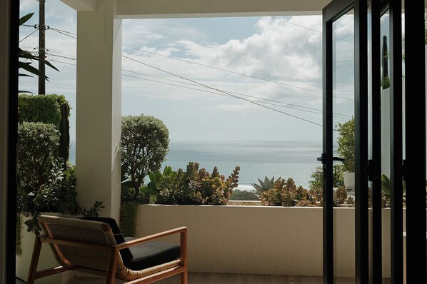 A balcony with a view of the sea, a chair, and a potted plant.