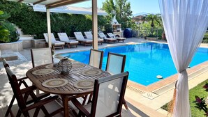 Et poolområde med en overdækket patio, liggestole og et spisebord med servietter.