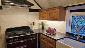A kitchen with a gas stove, wooden cabinets, a window with a view, and a potted plant. - Beautiful historic cottage pets welcome (Birchington-on-Sea)