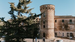 A historic tower with a round base and a square top, surrounded by trees and buildings. - Tower of Bassano Luxury Room (Vasto)