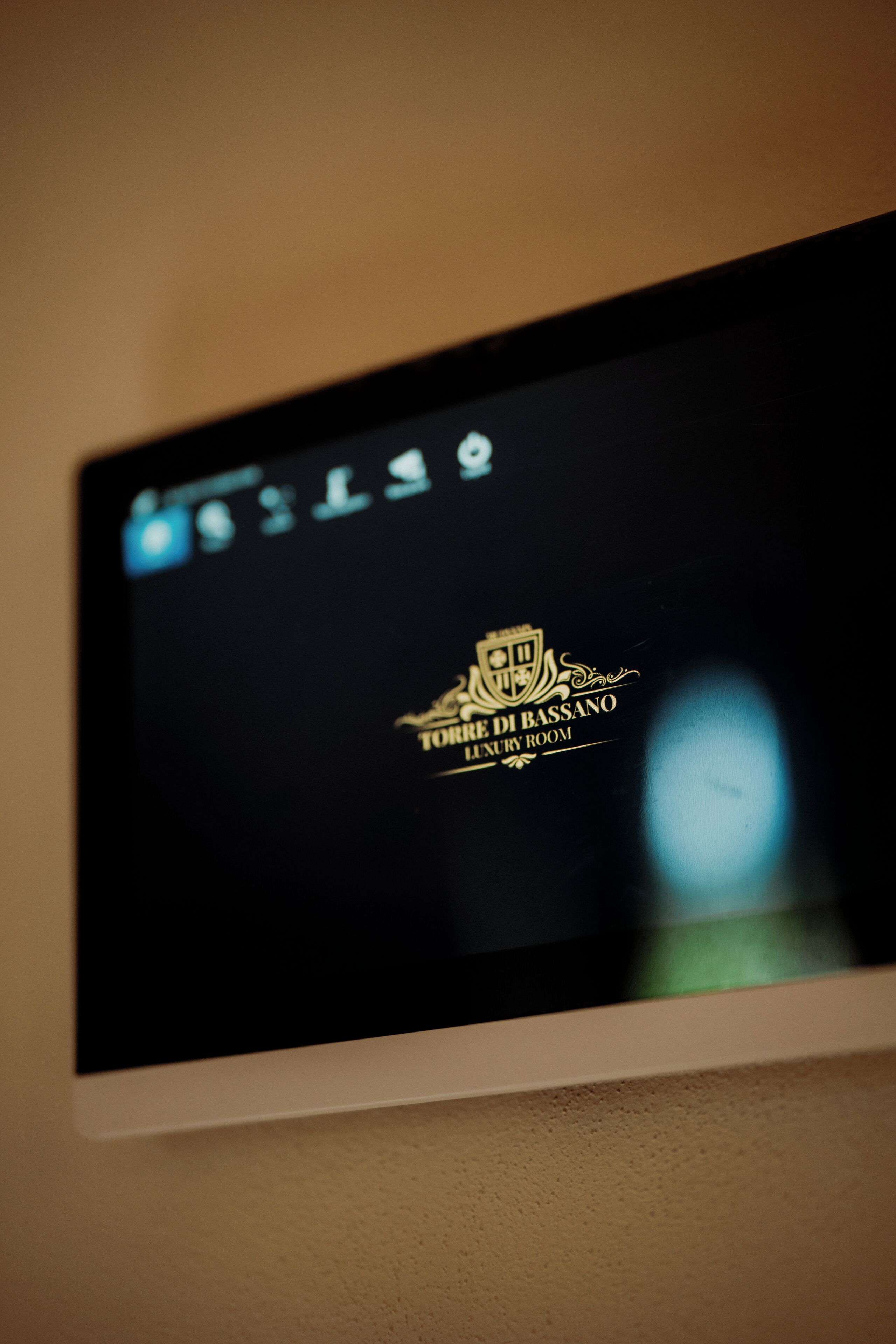 A television screen displaying the logo and name of a luxury room, "Torre di Bassano Luxury Room."