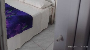 Une petite chambre avec un lit simple, un lit blanc et une couverture violette. Un appareil de climatisation blanc est fixé au mur, au-dessus du lit.