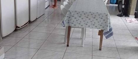 Una cocina con electrodomésticos blancos, una mesa de comedor con mantel y piso de baldosas.