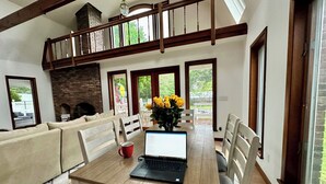 A dining area with a wooden table, chairs, a laptop, and a vase of yellow flowers.