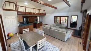A spacious living area with a wooden ceiling, a kitchen with wooden cabinets, a beige sectional sofa, and a dining table with chairs.