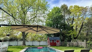 A backyard with a swimming pool, lounge chairs, a red shed, and a pergola.